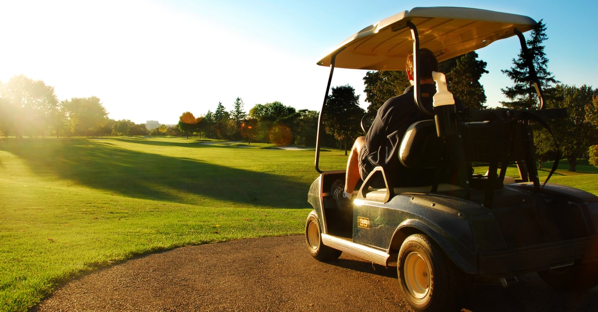 Ein Mann sitzt in einem Golfcart während eines Sonnenuntergangs