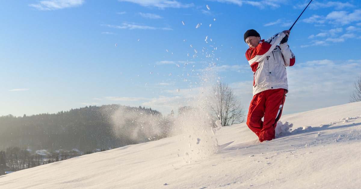 Ein Golfer in Winterkleidung schlägt einen Golfball im Schnee