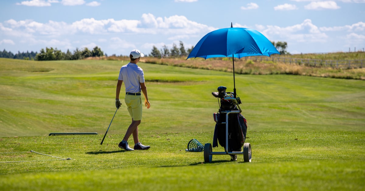 Ein Mann macht sich auf dem Golfplatz zum Abschlag bereit, sein Golfbag wird durch einen Golfschirm geschützt.